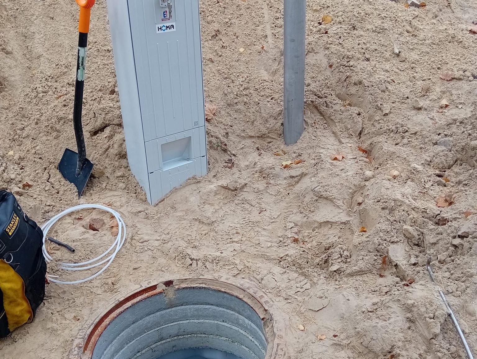 Eine Kasten mit der Aufschrift "HOMA" neben einem offenen Kanaldeckel